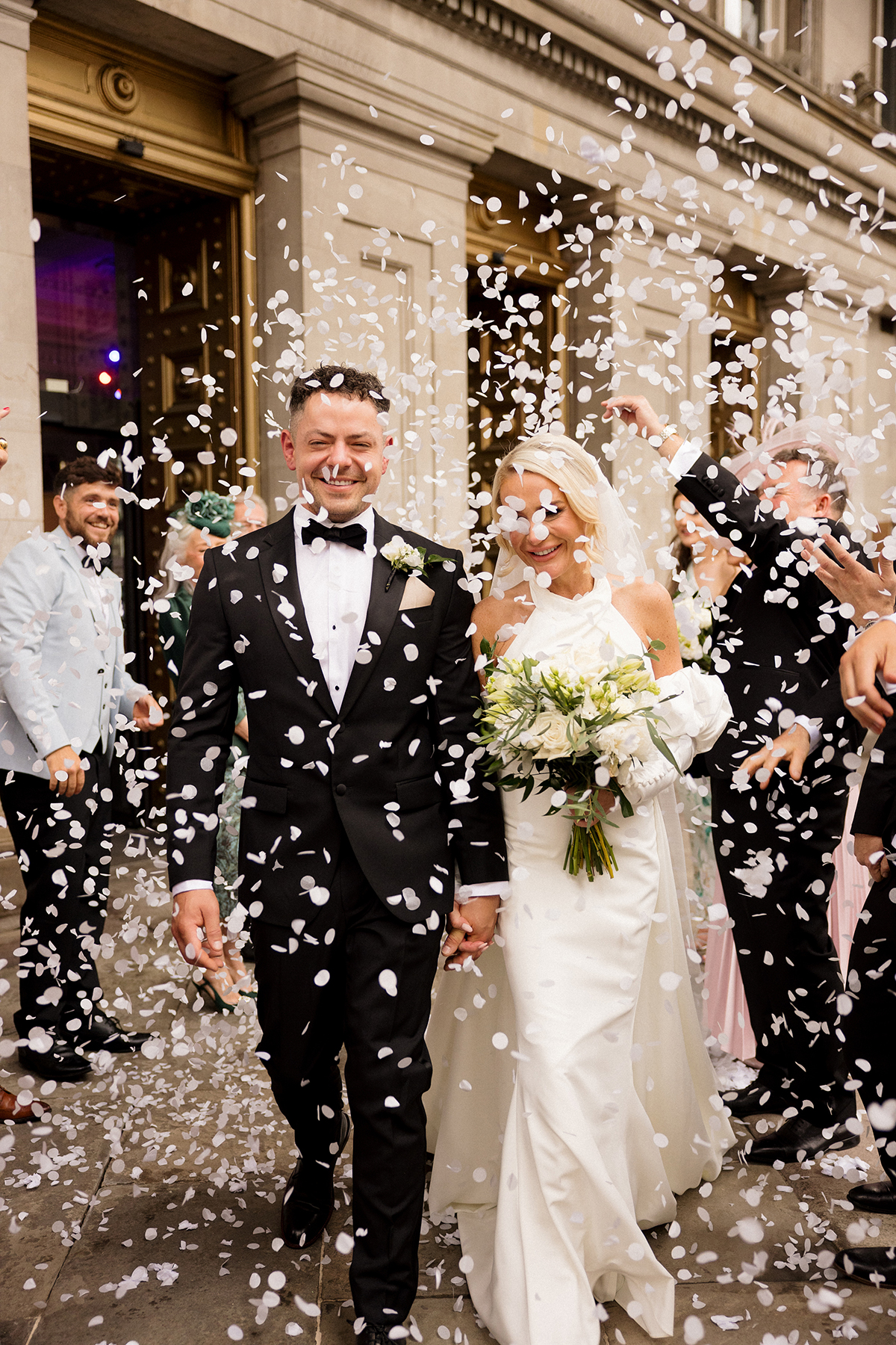 Bride and groom walking through white confetti outside The Exchange in Glasgow