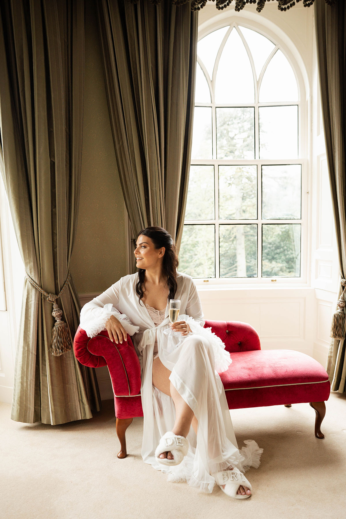 Bride getting ready in bridal robe sitting on chaise longue with champagne at Drumtochty Castle Aberdeenshire wedding