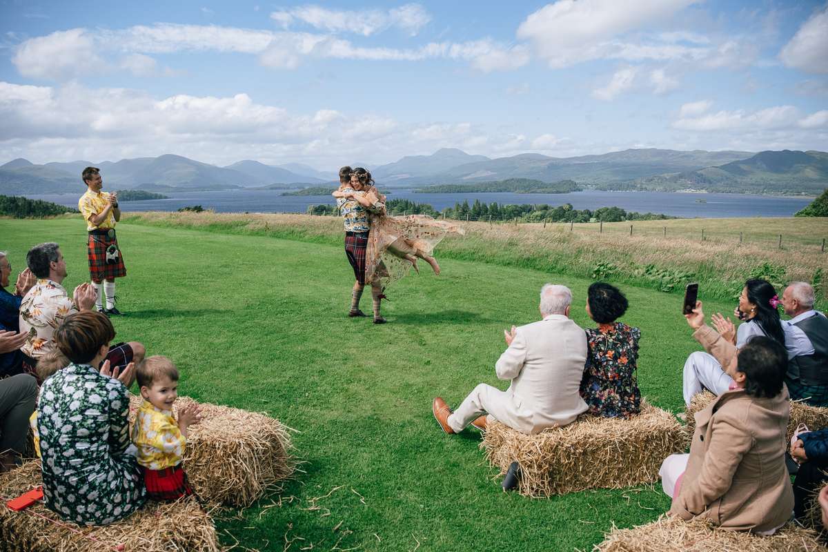 Groom lifting his bride during an outdoor wedding ceremony at Ardoch Loch Lomond