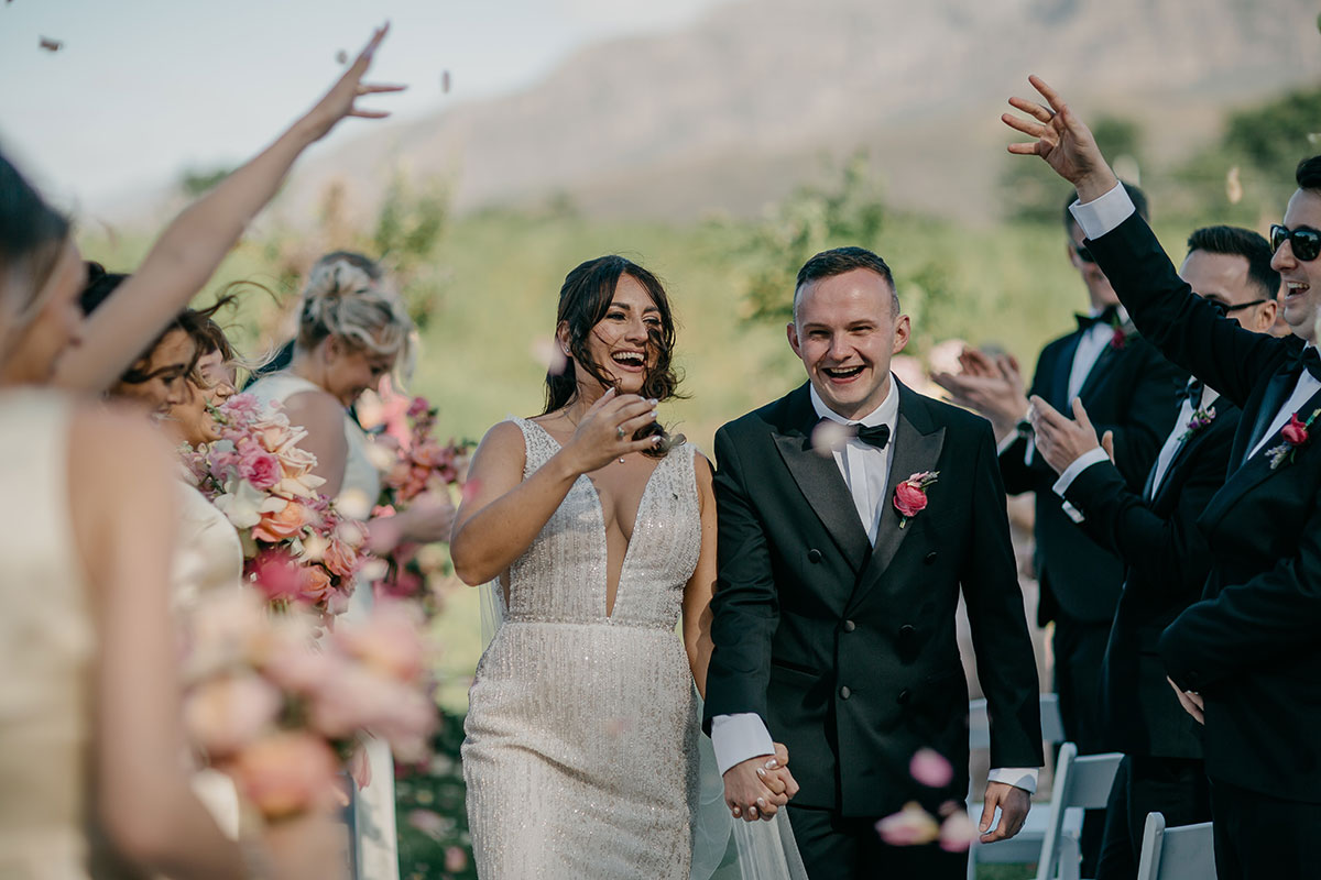 Bride and groom walking through rose petal confetti after their outdoor ceremony at Boschendal Wine Estate, Cape Town