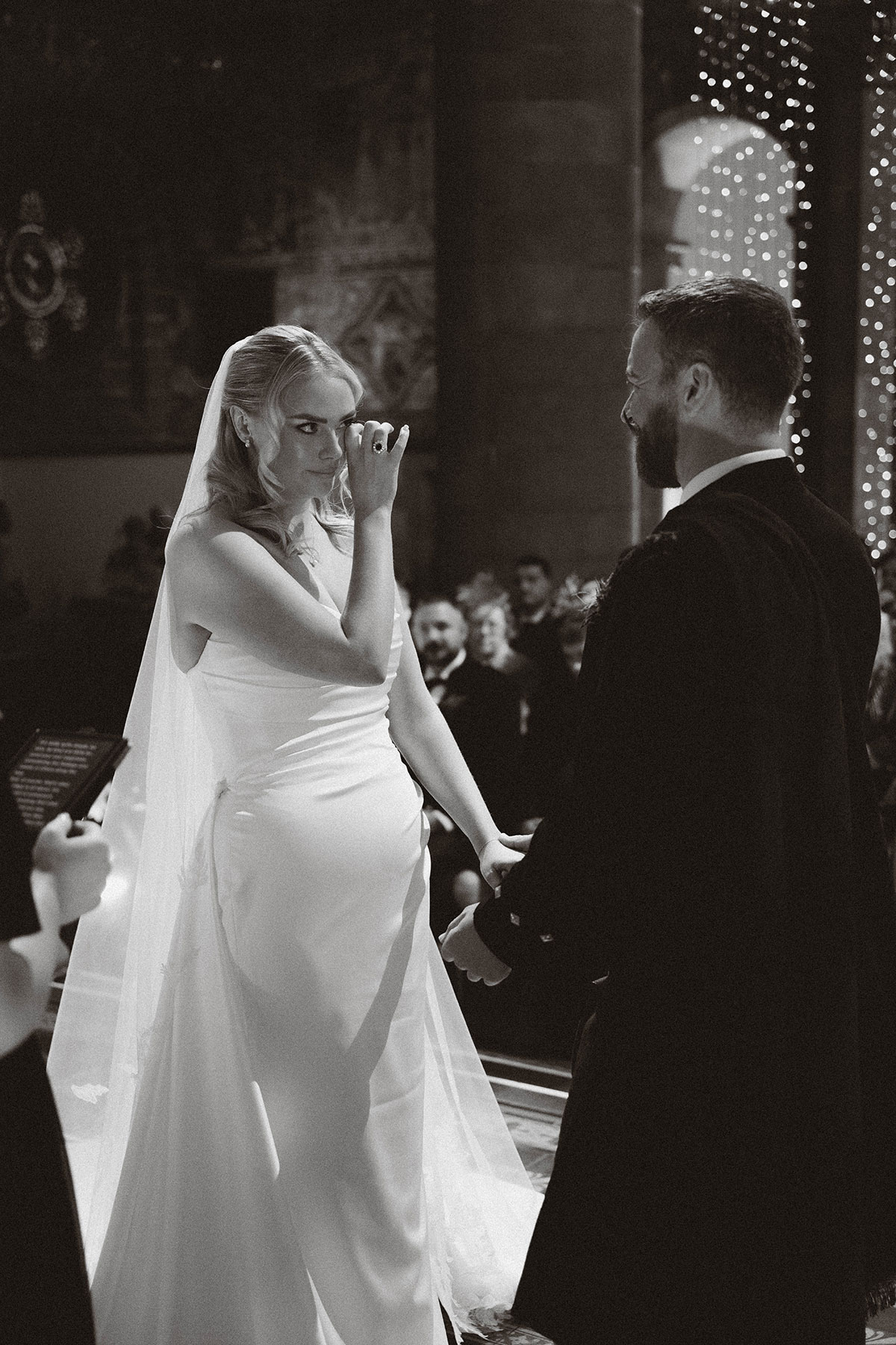 bride wiping tears during ceremony while holding hands with groom