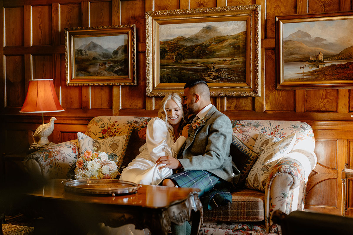 Bride and groom relaxing on a sofa in a wood-panelled lounge during their Scottish wedding day