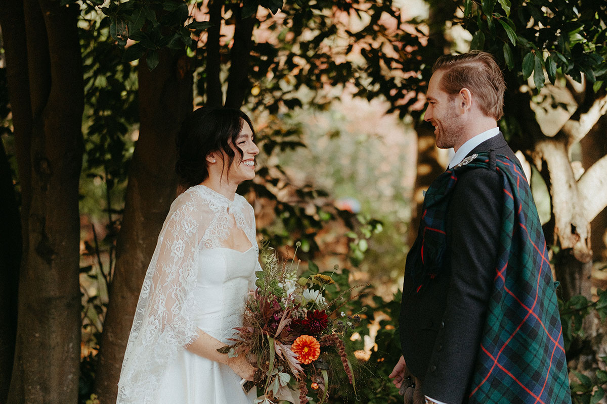 Bride laughs during an intimate first look with the groom beneath the trees at Cambo Country House in Fife.