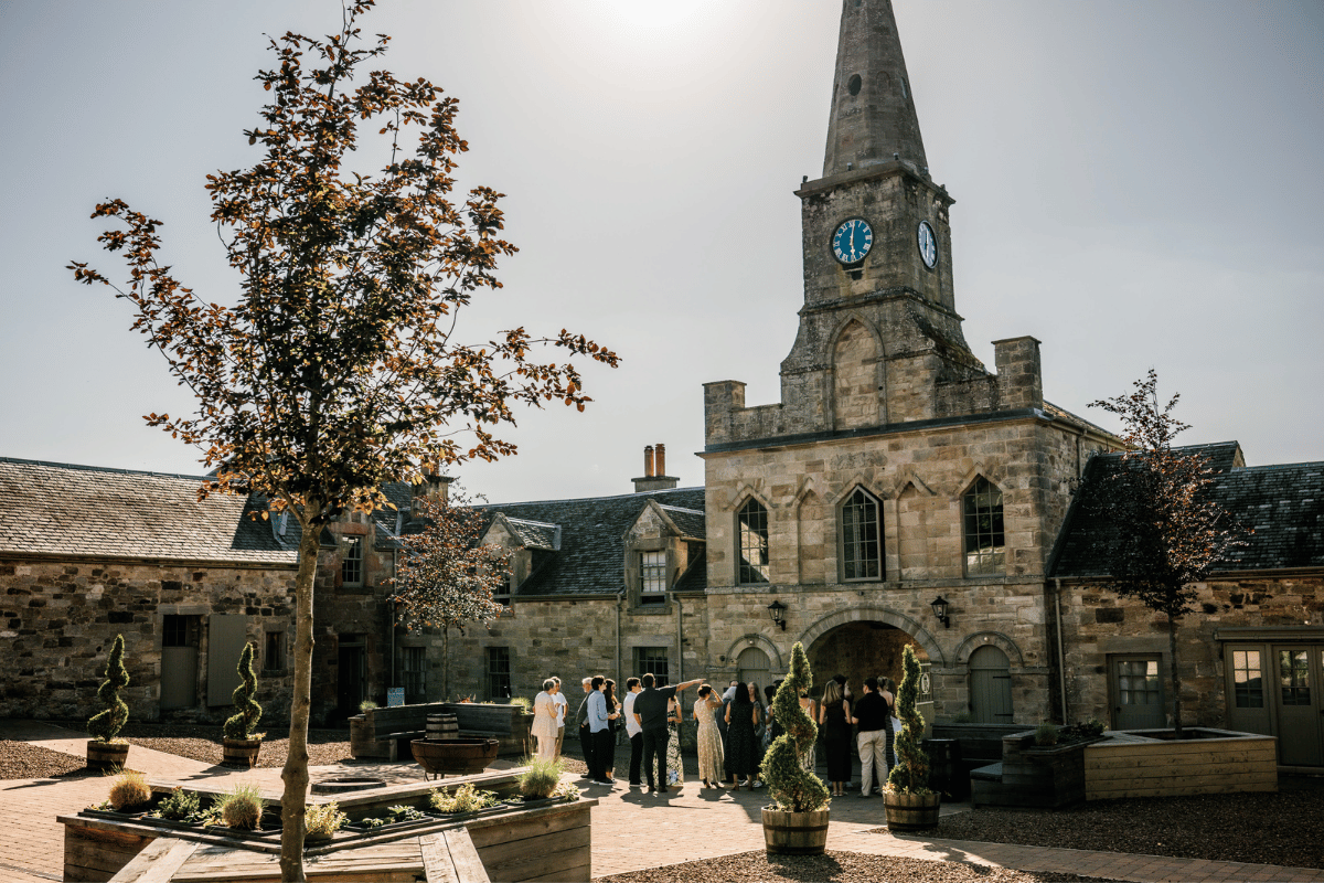 Wedding guests gathered in the courtyard at Rosebery Steading beneath the venue’s stone clock tower