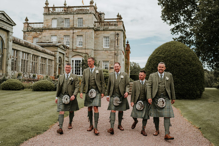 five men wearing green kilts walking along a path towards the camera