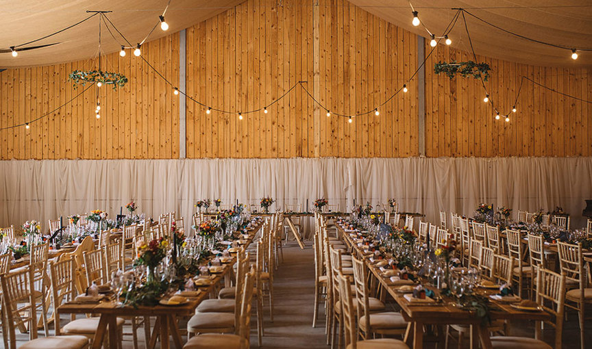 The Barn at Carrick Castle with wooden clad walls, set with long tables and chiavari chairs for a wedding dinner
