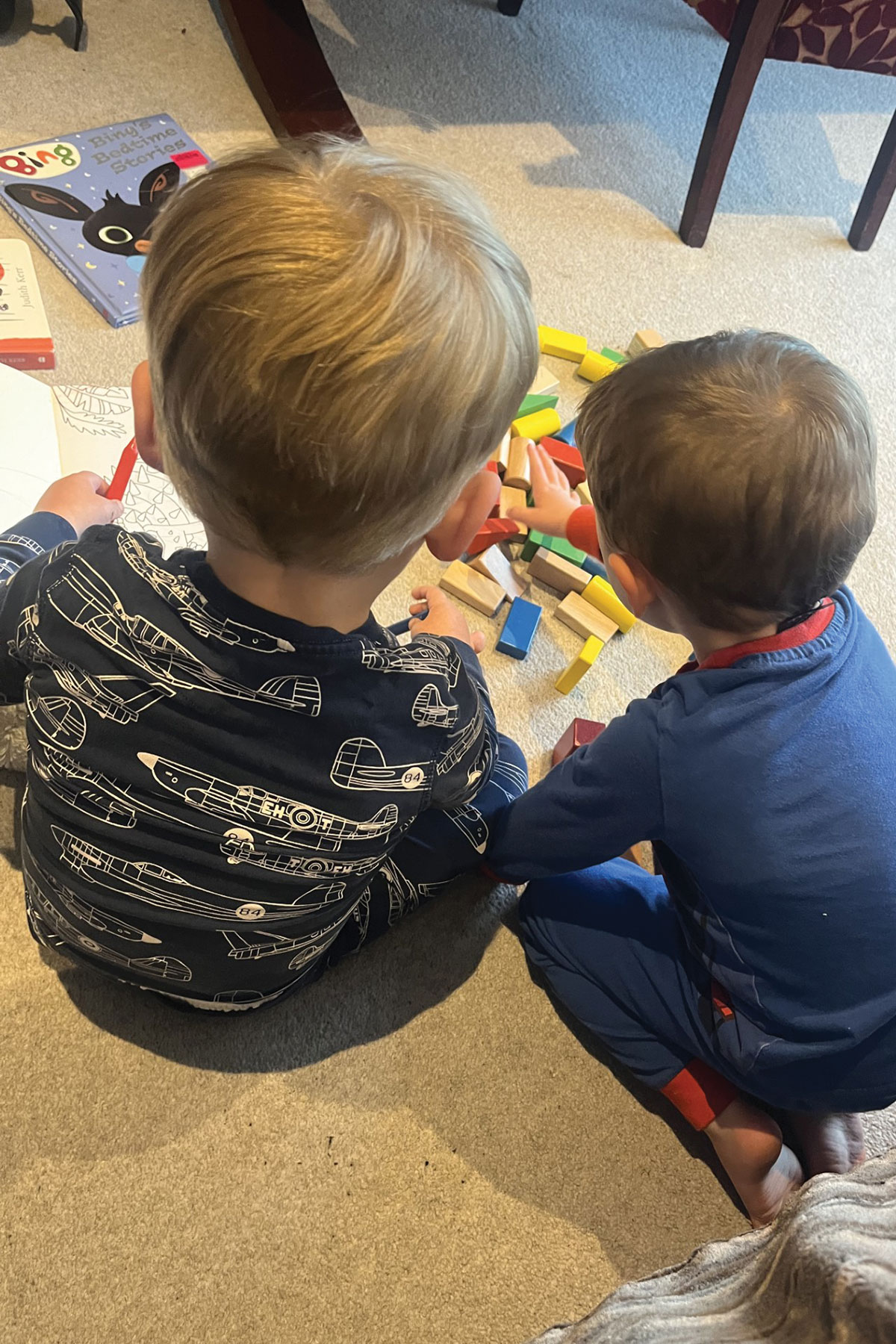 two small boys sit on carpet in their pyjamas colouring and playing with colourful wooden blocks