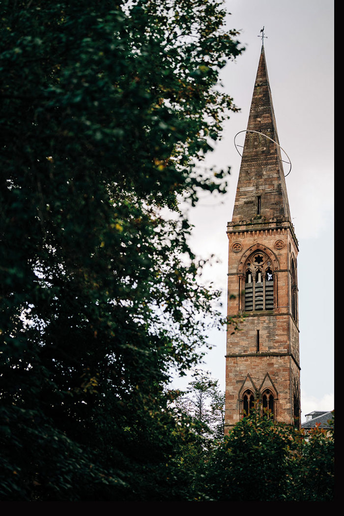 a tall slender stone bell tower peeking out on the right side, behind a large gathering of dense trees