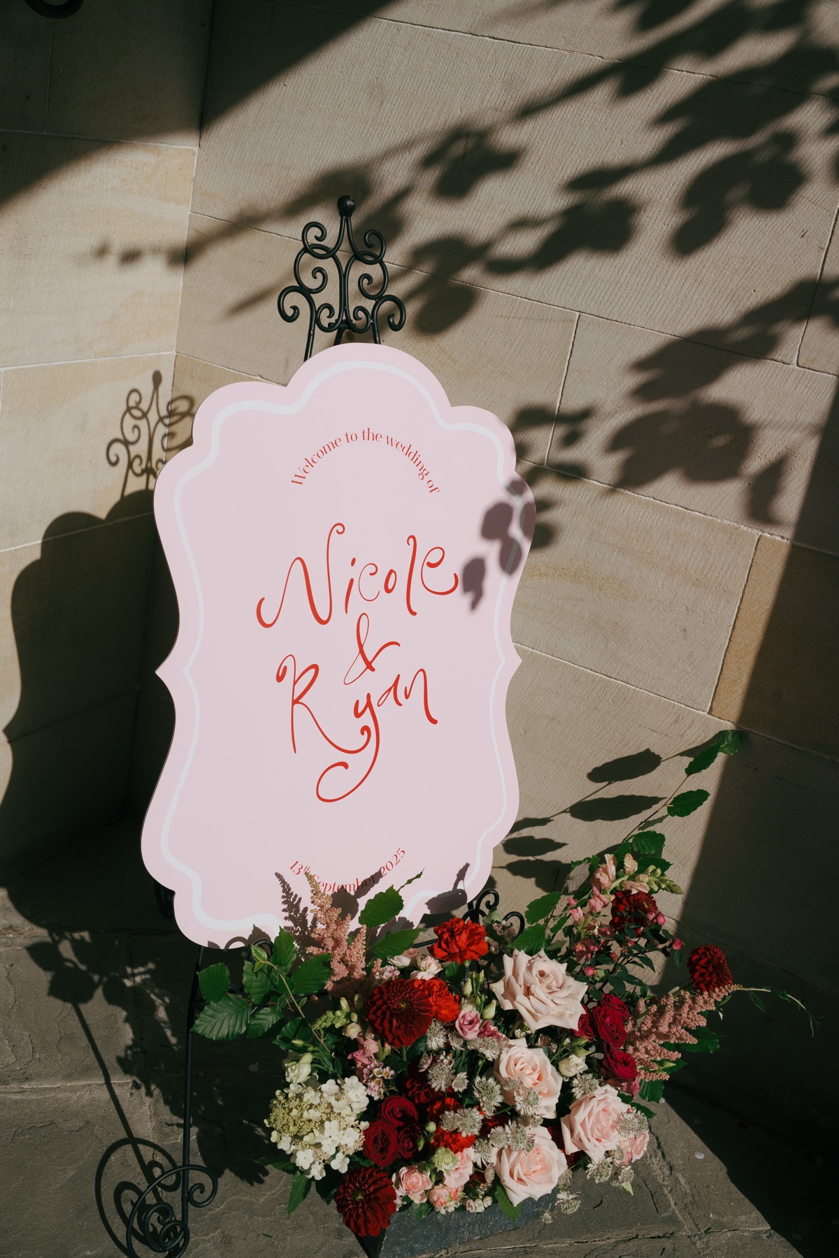 Personalised pink welcome sign for Nicole and Ryan's wedding at Barnbougle Castle, surrounded by red, blush pink and ivory flowers.
