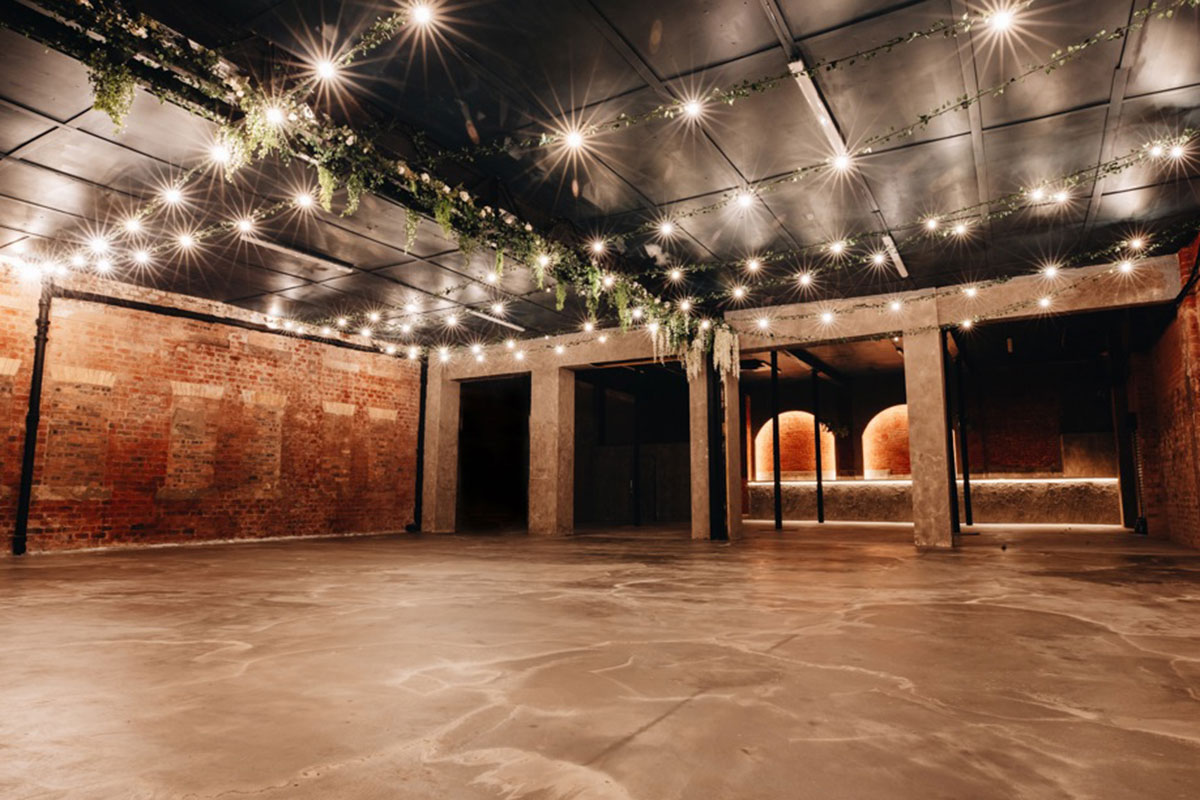 a large empty events space with brick walls and a paneled ceiling complete with draped foliage and twinkle lights