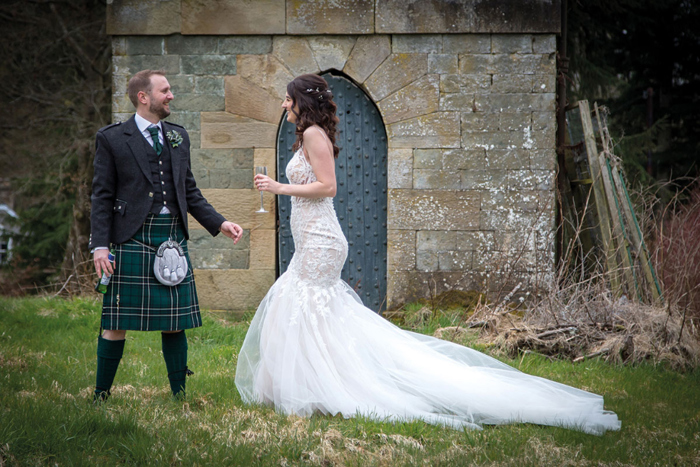 a man in a kilt and a woman in a white wedding dress standing on grass 