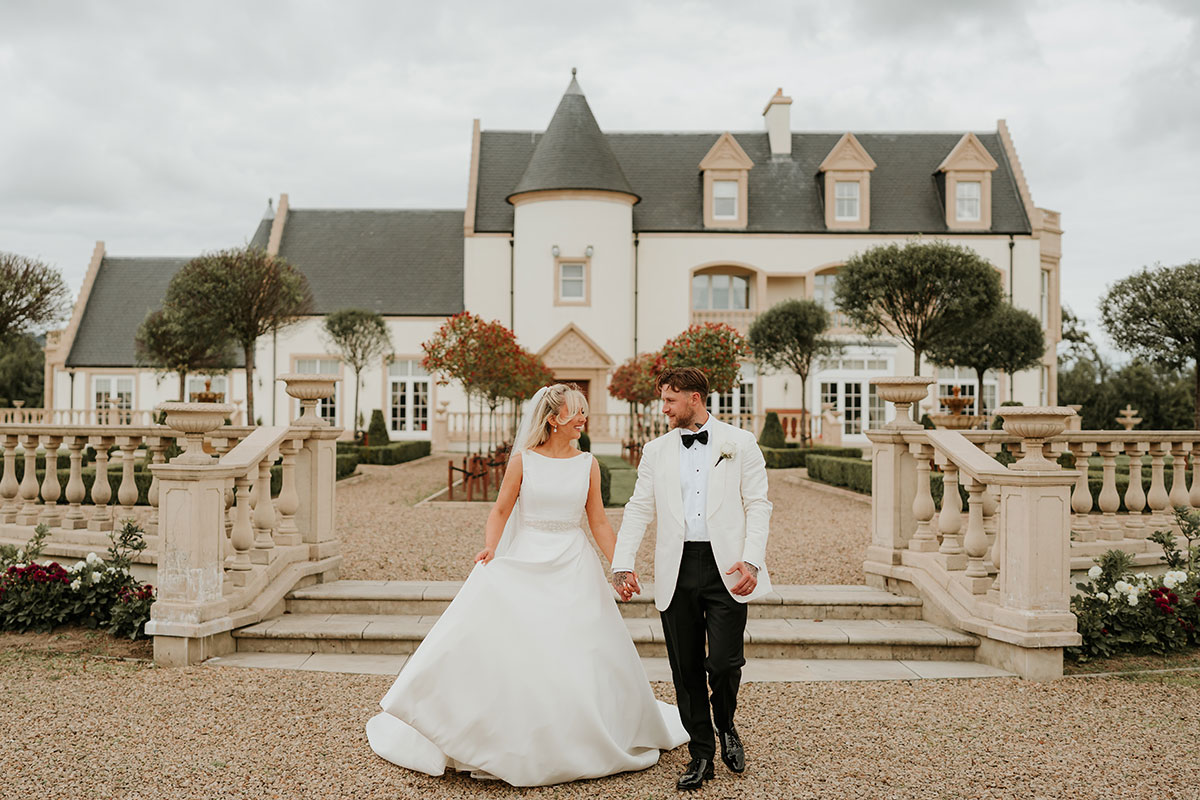 Newlyweds walking hand in hand in front of Ingliston Country Club exterior