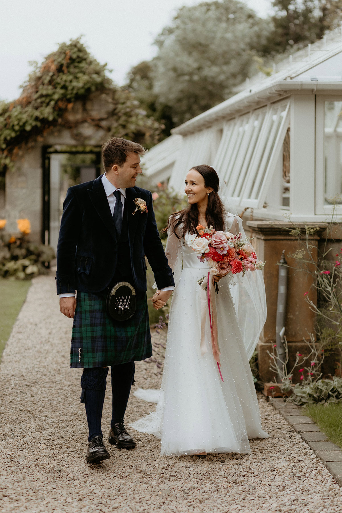 a bride and groom walking hand in hand beside a white glasshouse at Carlowrie Castle