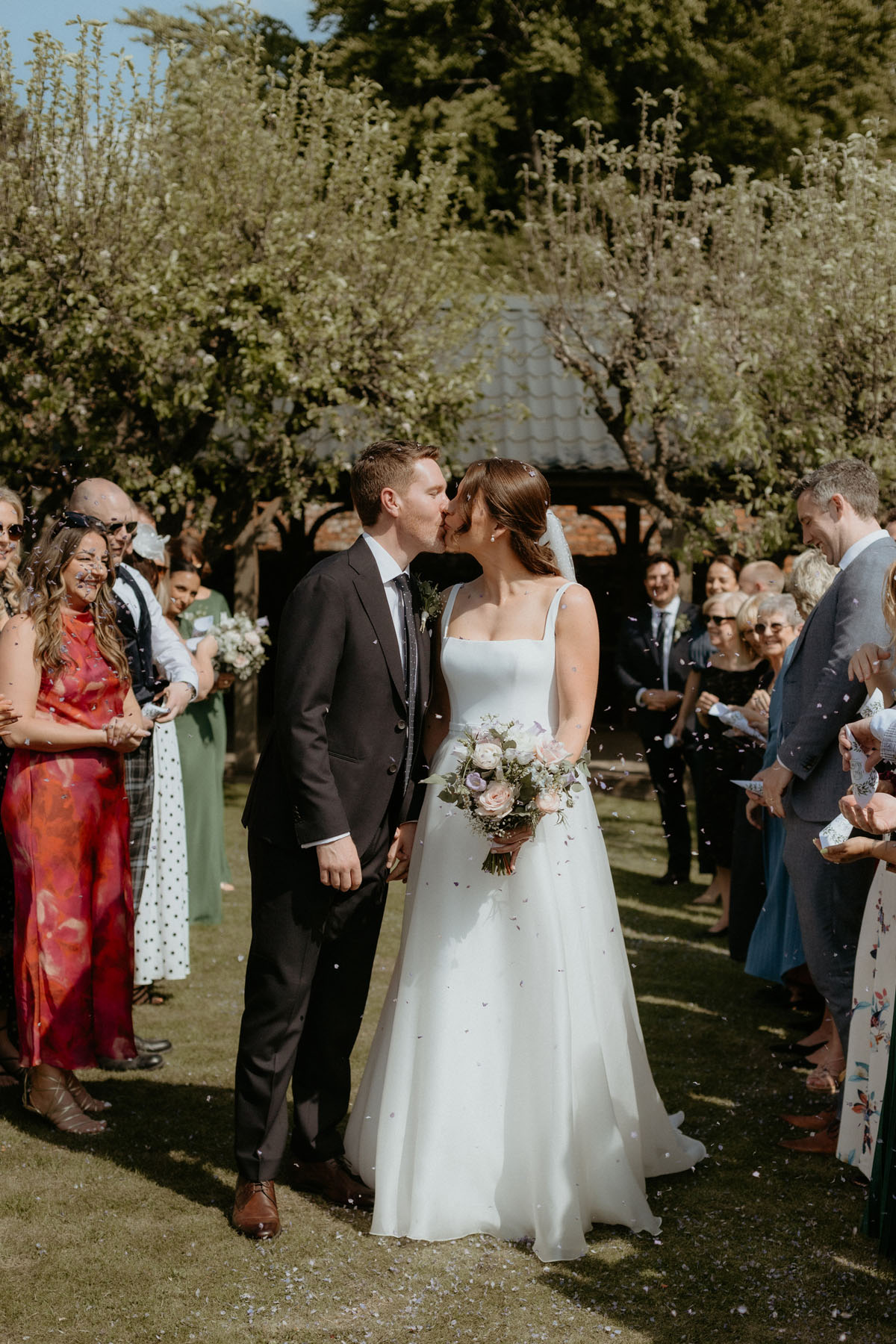 Newlyweds kissing as guests throw confetti after their wedding ceremony at The Byre at Inchyra.