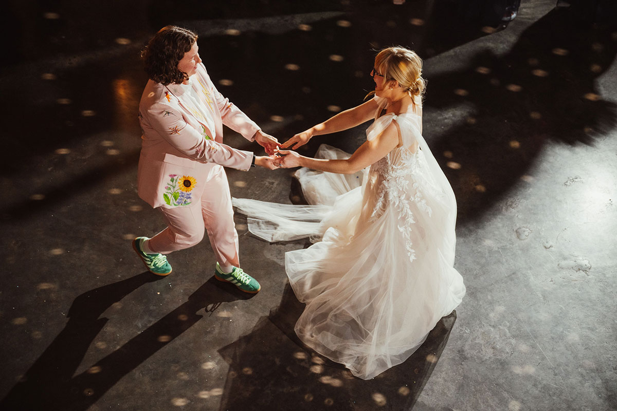 The newlyweds dancing together under disco lights at the Engine Works, one wearing a pink embroidered suit and the other in a flowing lace dress.