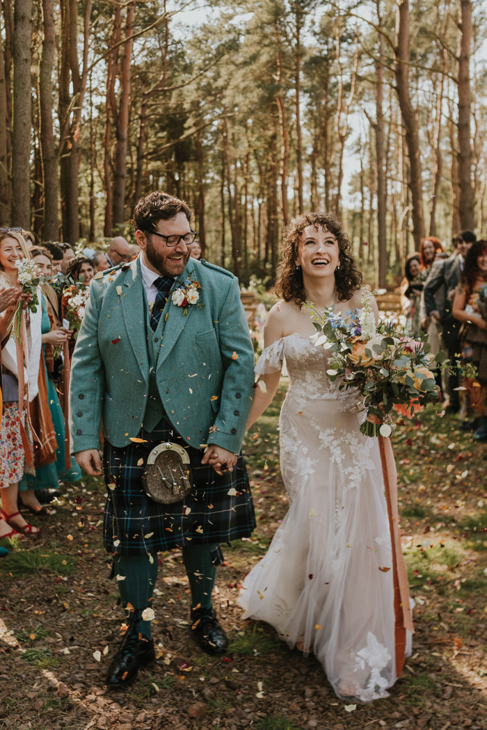 bride holds large flower bouquet as she smiles at camera with husband after marrying outdoors