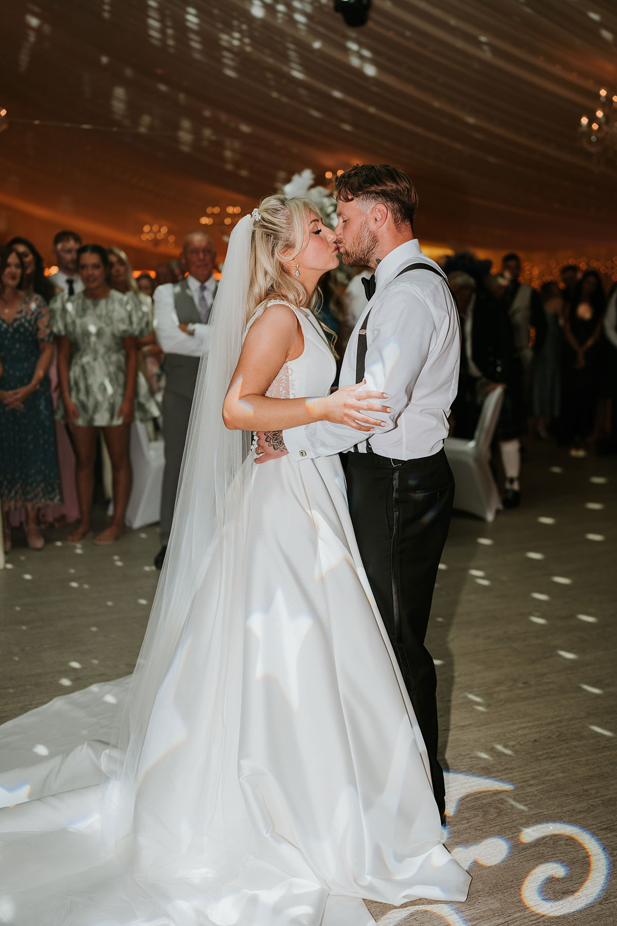 Bride and groom kissing during first dance surrounded by guests at Ingliston Country Club reception