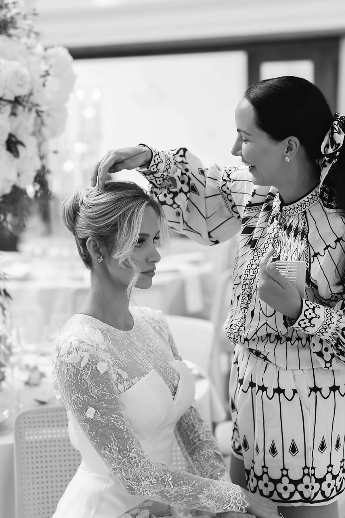 Black and white photo of hairstylist styling bride’s hair before wedding ceremony