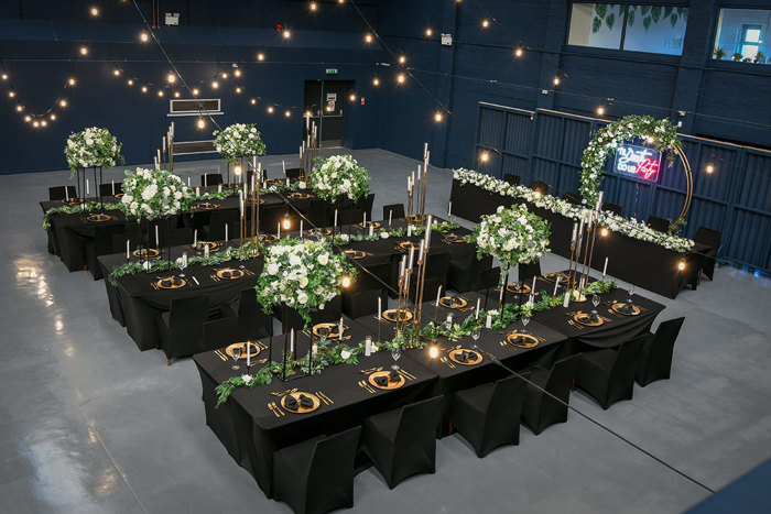 large open wedding venue set with long black dining tables set up with tall candle sticks and white and green floral arrangements