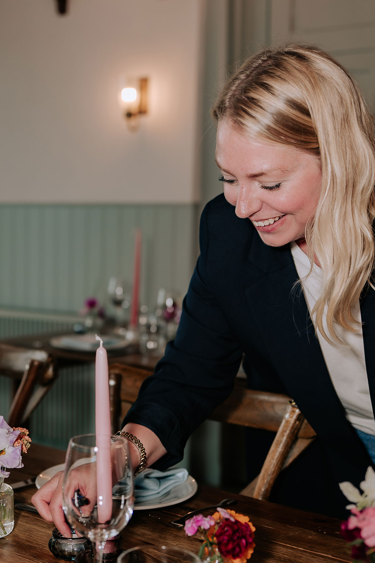 Wedding stylist placing glassware on a styled reception table with pink taper candles and floral details
