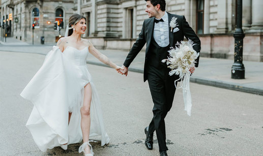 A bride and groom walk through a city holding hands 