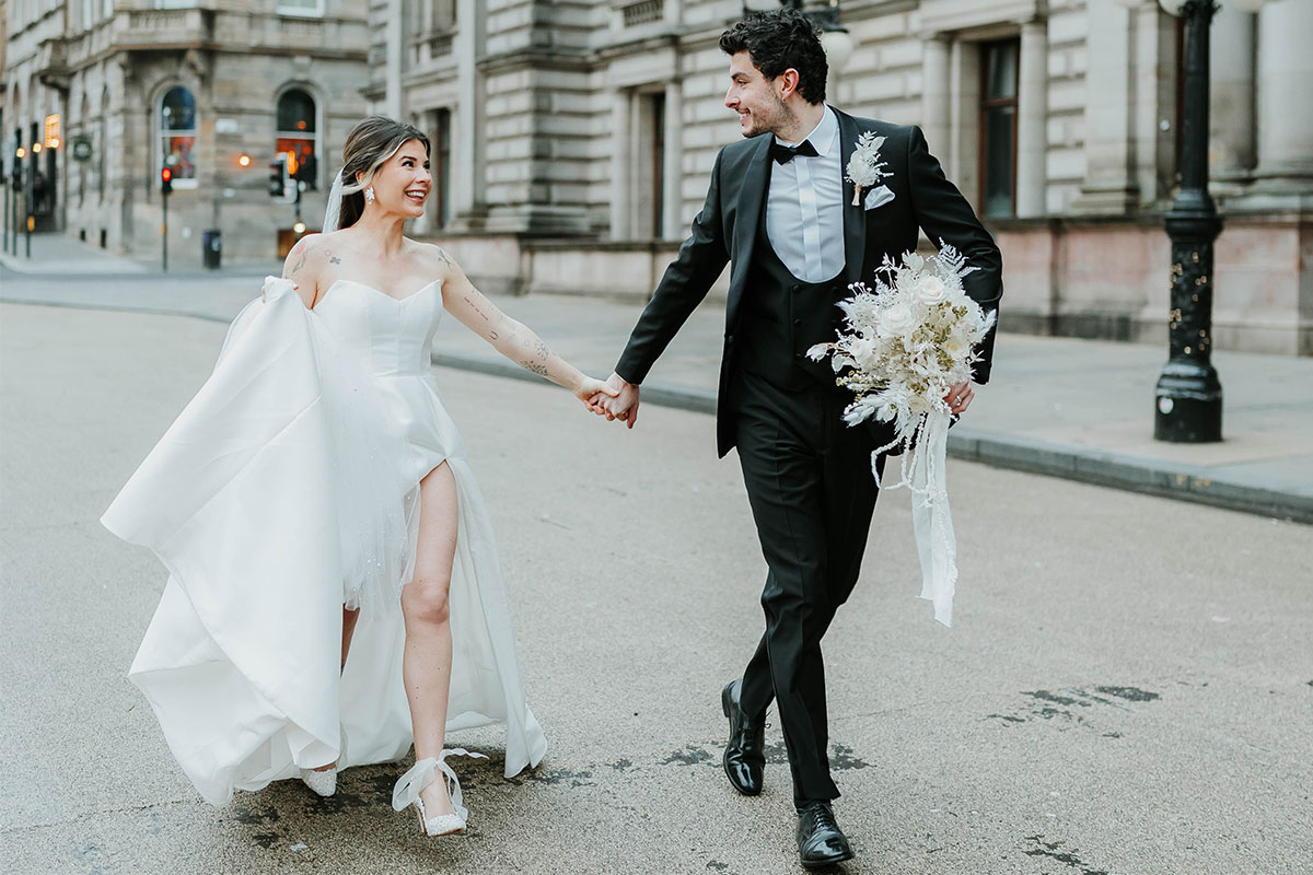 A bride and groom walk through a city holding hands