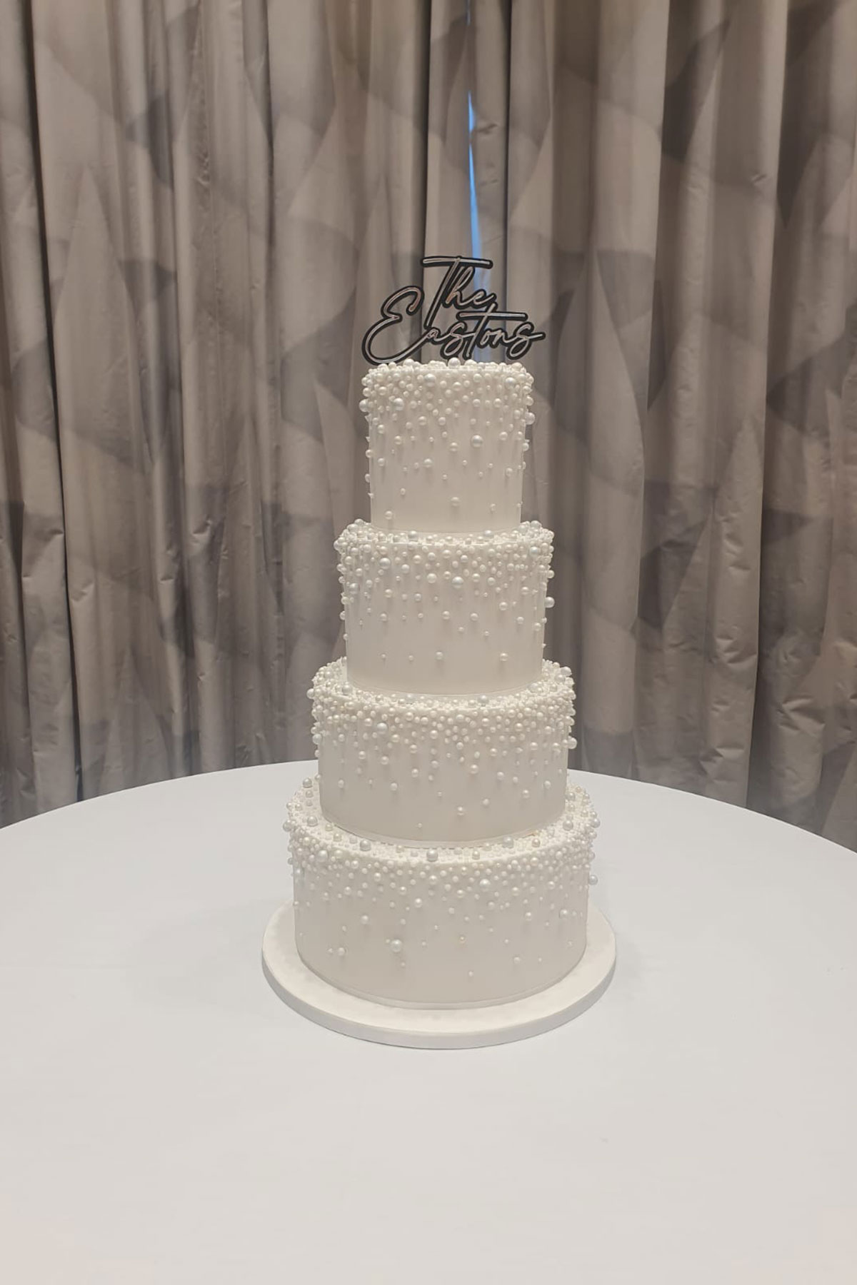 four-tier wedding cake covered in differently sized pearls and topped with a black and silver 'The Eastons' cake topper