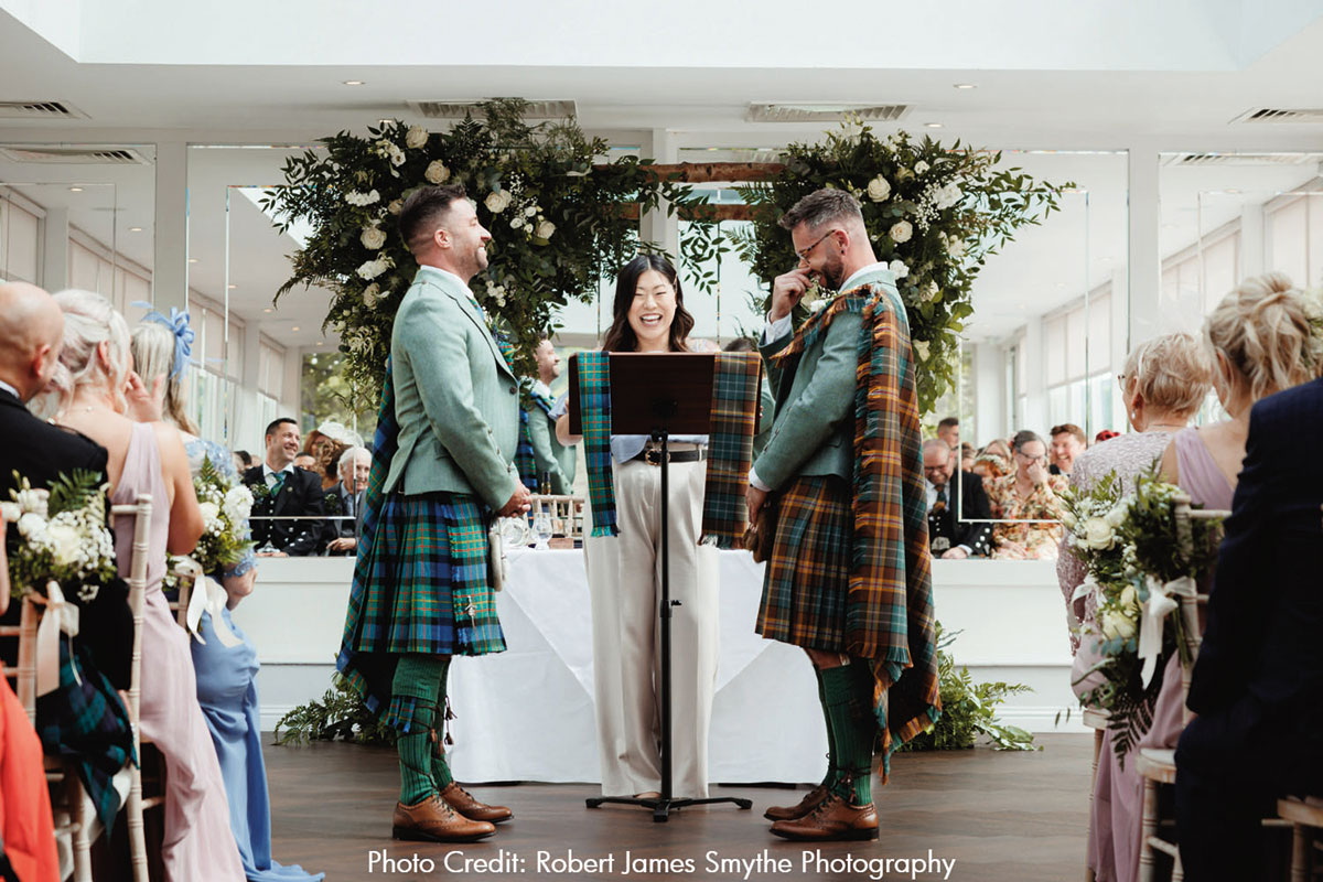 Two grooms and celebrant at the top of the aisle