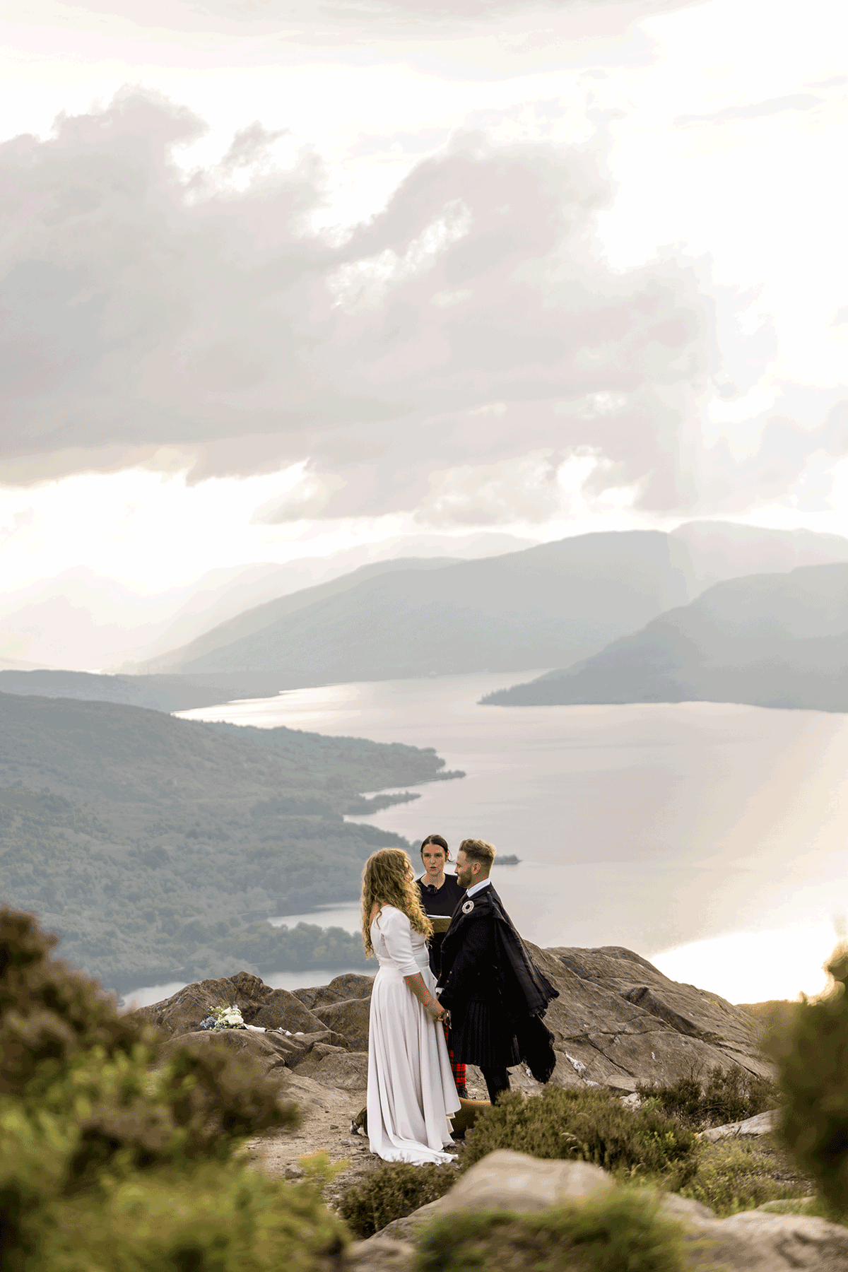 Couple exchange vows on a mountaintop overlooking a loch and mountains during an intimate Scottish Highlands wedding ceremony