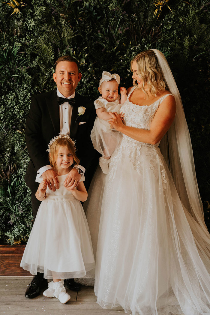 A bride and groom in wedding attire with two children.