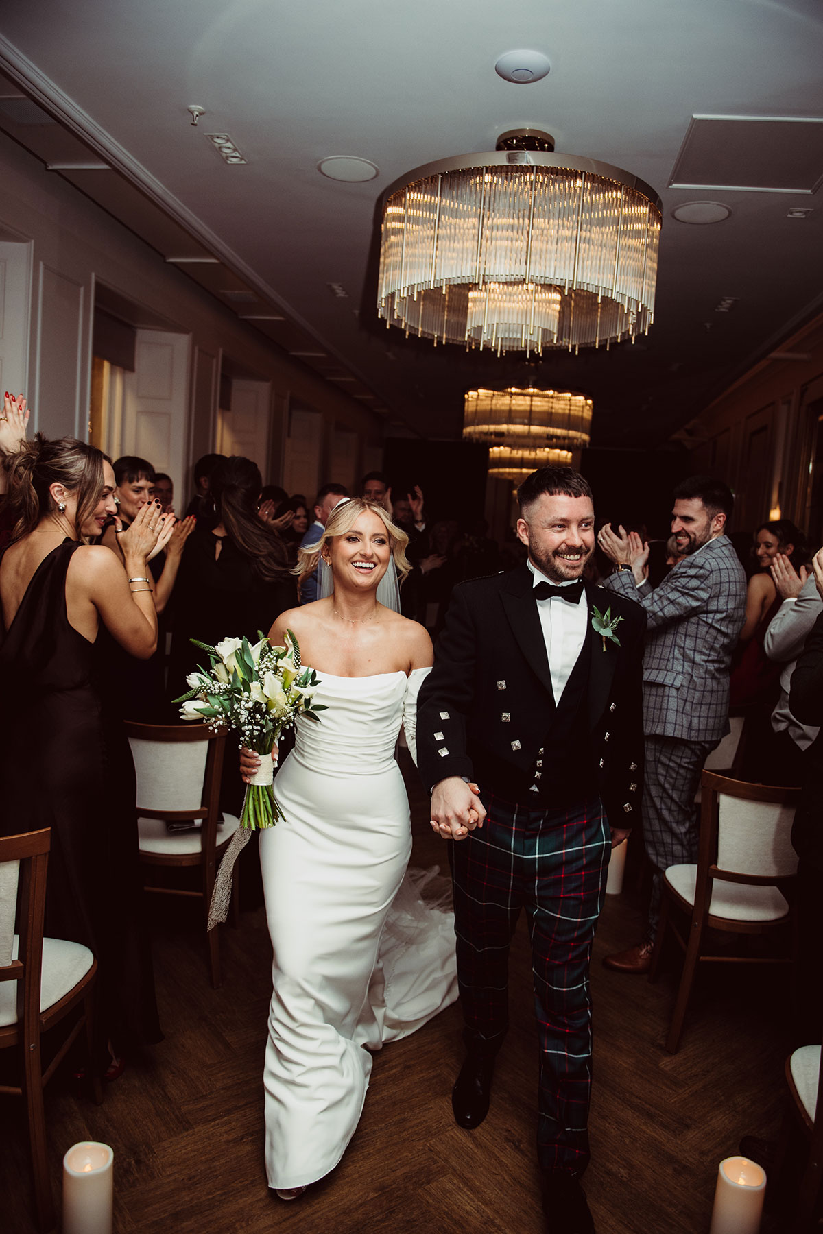 Bride and groom walking hand in hand down the aisle indoors as guests stand and applaud