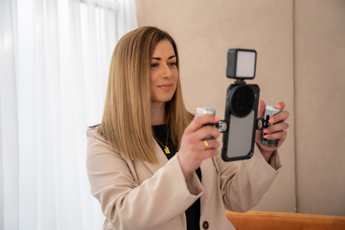 Woman wearing cream blazer holding phone with filming device attached