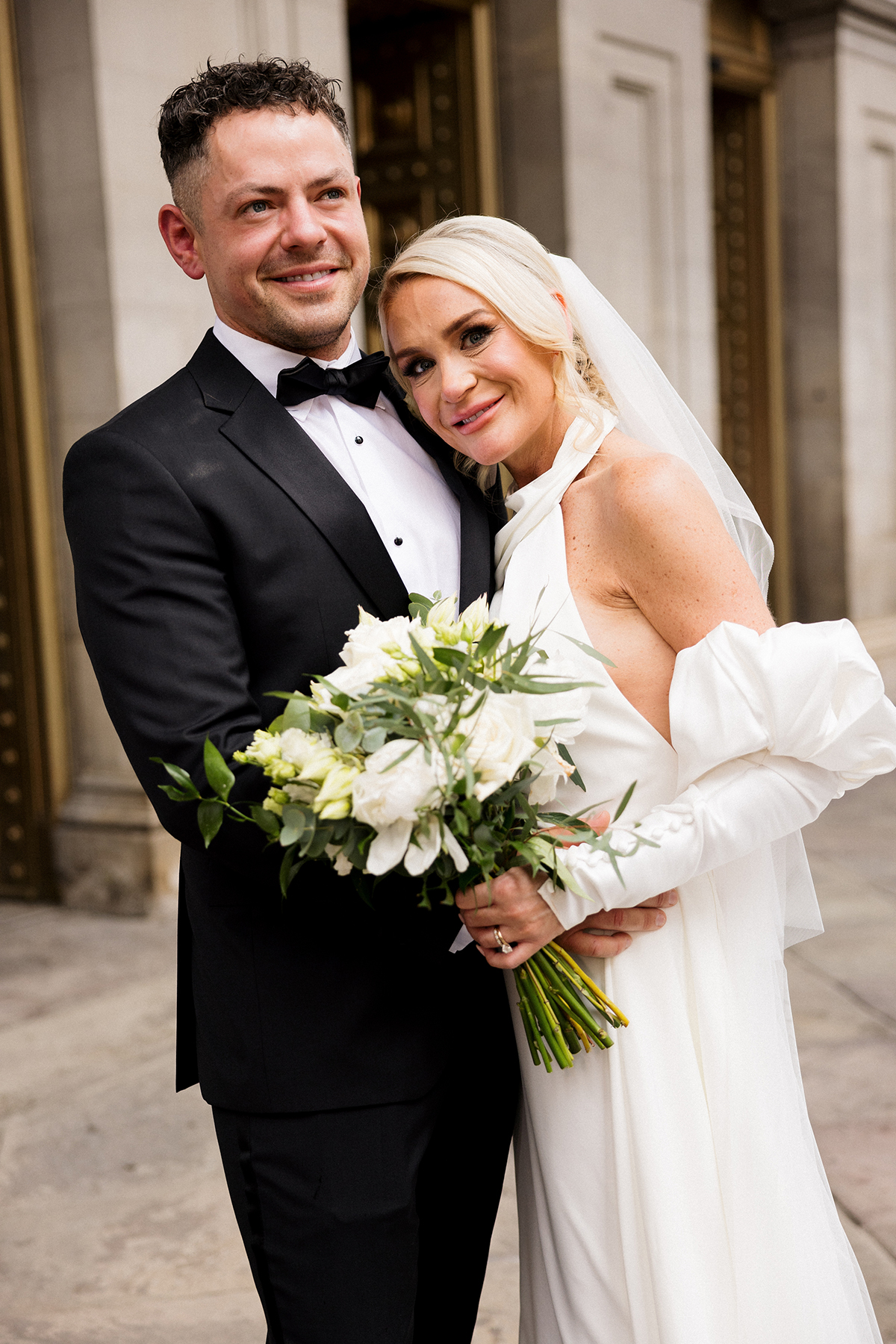 Bride and groom posing with a white bouquet outside after their city wedding ceremony