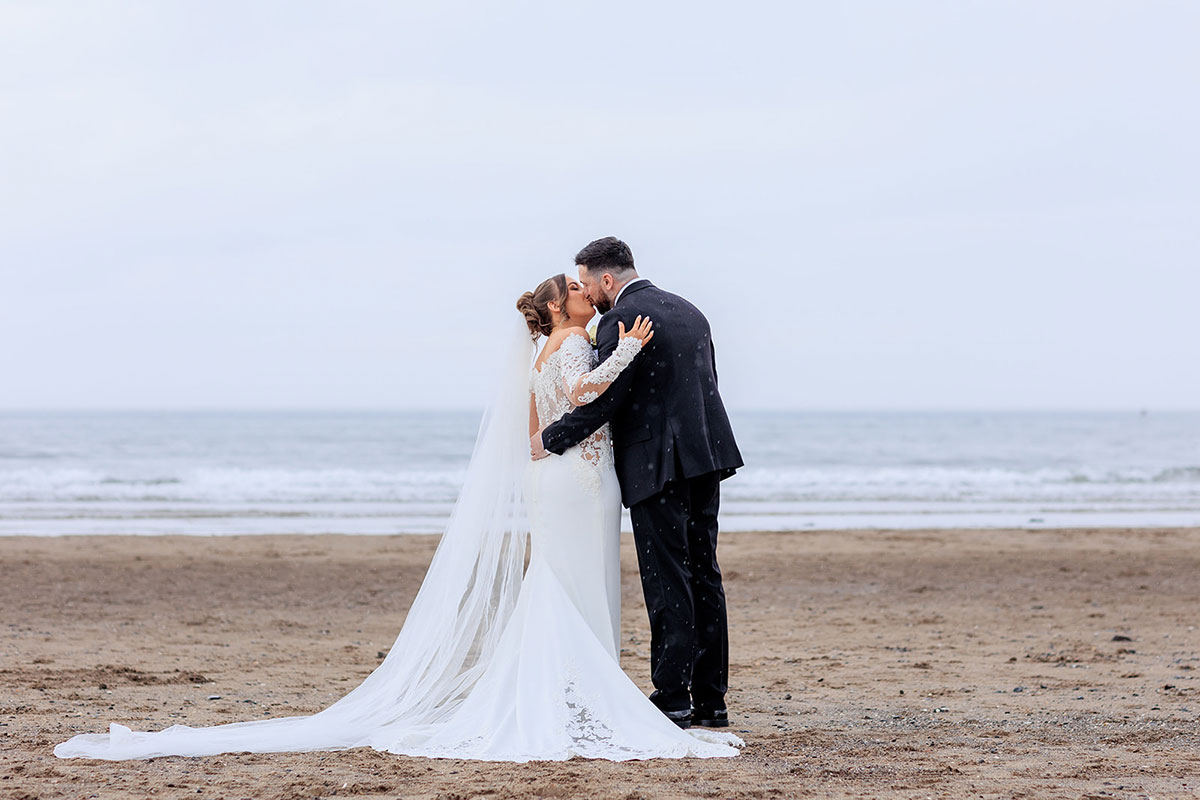 Bride and groom kissing on the beach near The Gailes Hotel & Spa, with the sea in the background.