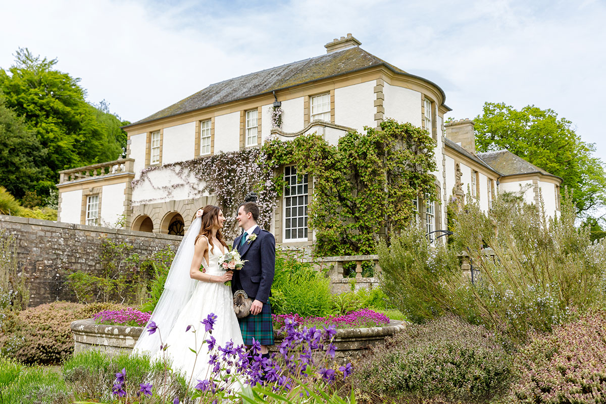 Bride and groom posing outside Hill of Tarvit house with climbing ivy and landscaped gardens in springtime