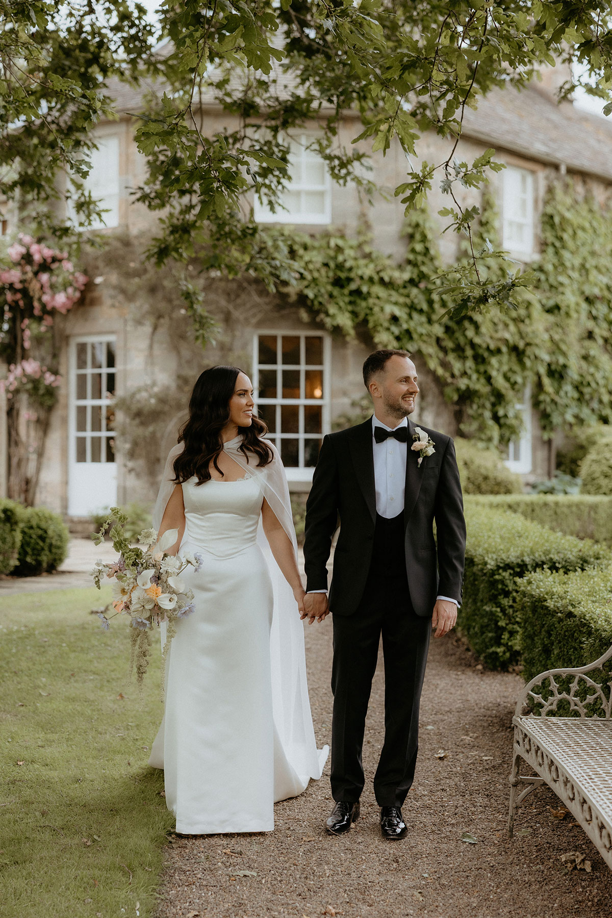 Newlyweds holding hands in formal gardens at Rosebery House and Steading, Midlothian summer wedding.