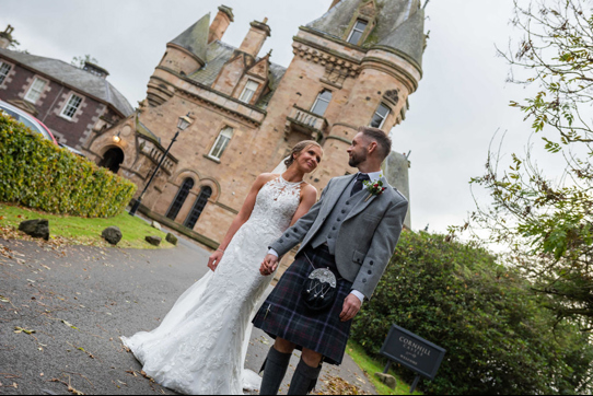 A Bride And Groom Walking With Cornhill Castle In Background