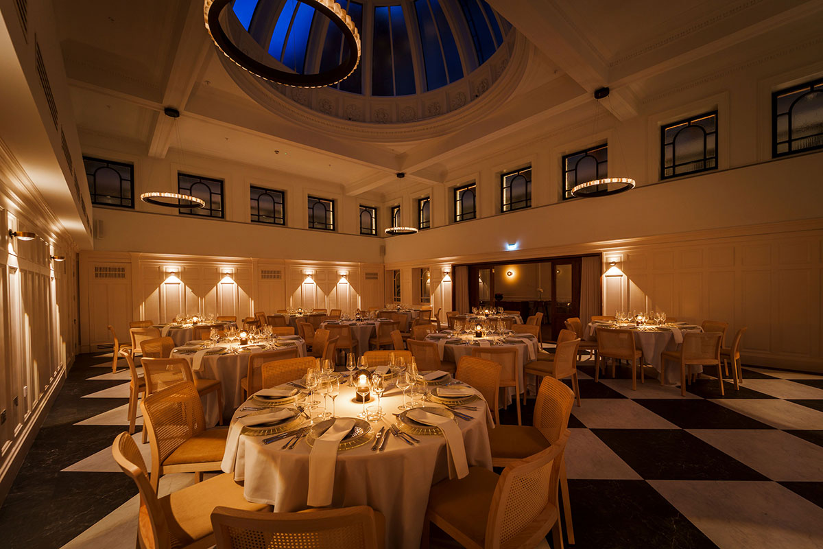 the collector's hall at night set up for a wedding dinner with checkerboard floor, cream linen and rattan chairs