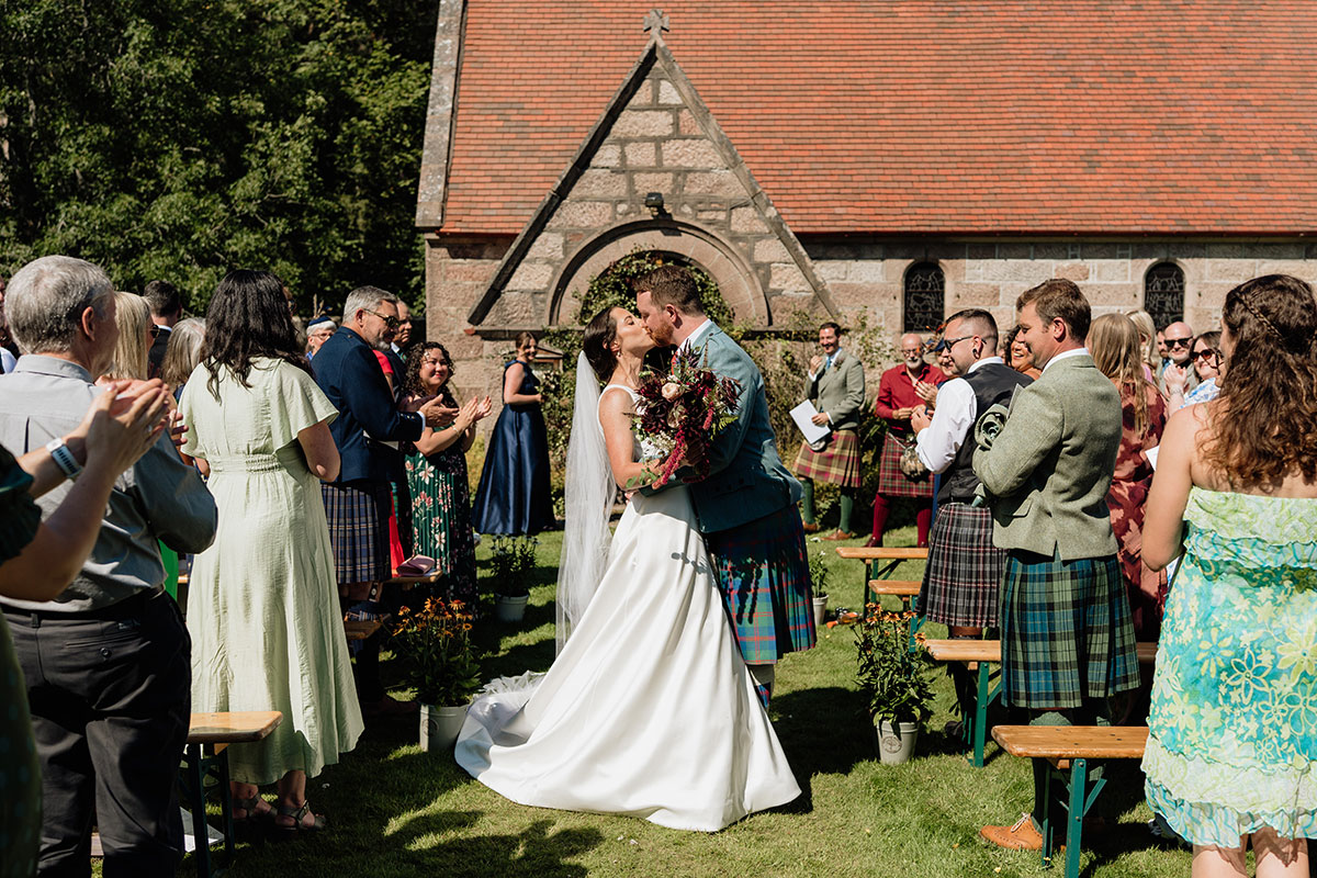 Bride and groom sharing their first kiss after an outdoor ceremony surrounded by wedding guests at Mar Lodge Estate
