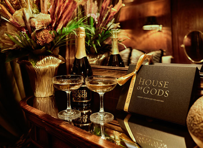 flowers and prosecco with prosecco glasses next to mirror and card that displays 'House of Gods' 