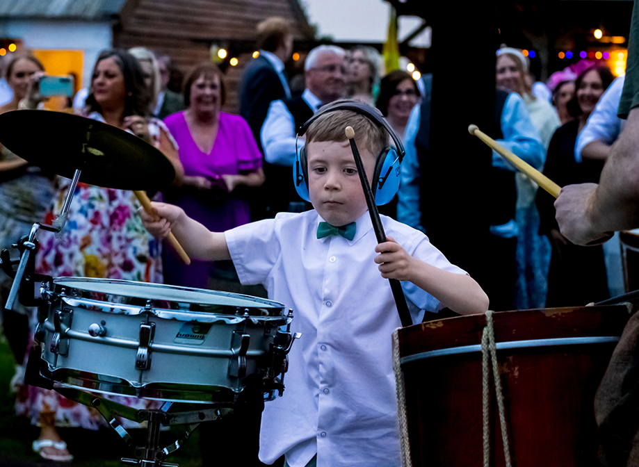 young boy wearing headphones and drumsticks playing drumkit
