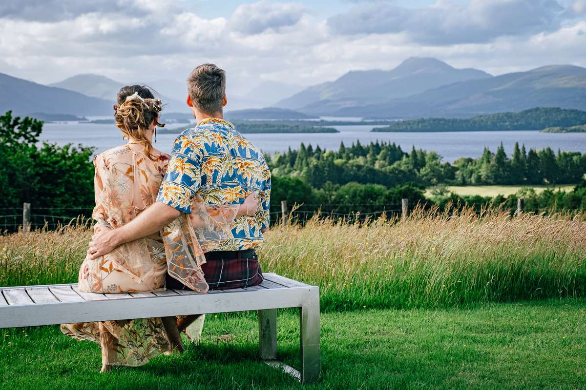 Newlyweds sitting together on a bench at Ardoch Loch Lomond looking towards the mountains