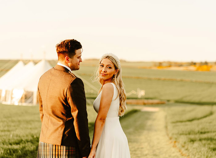 a bride and a groom bathed in golden light at sunset in a field with a marquee in the background