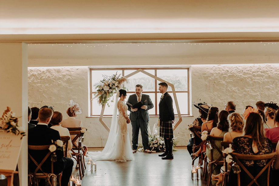 A bride and groom during their ceremony inside a barn