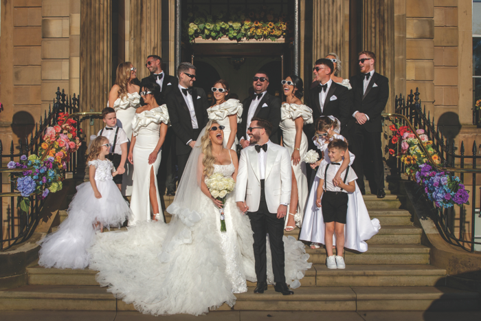 Bride and groom with bridal party standing on sandstone stairs all wearing sunglasses