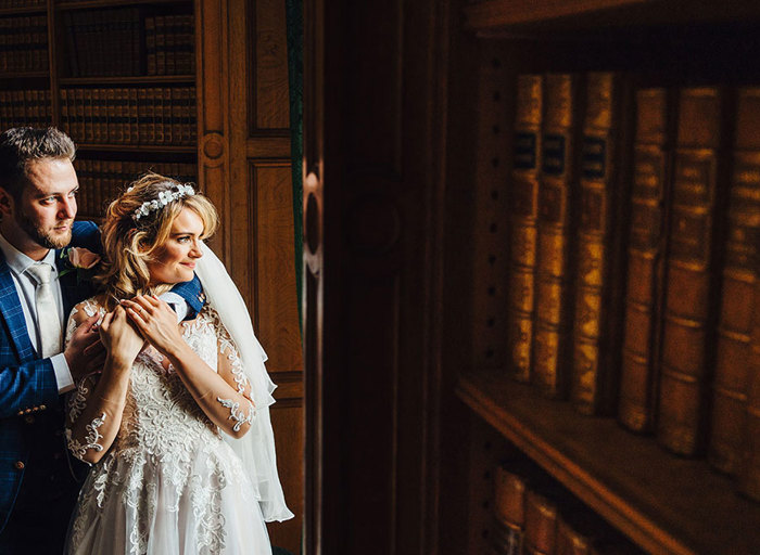 Bride and groom look away from camera next to a close-up of a shelf of library books