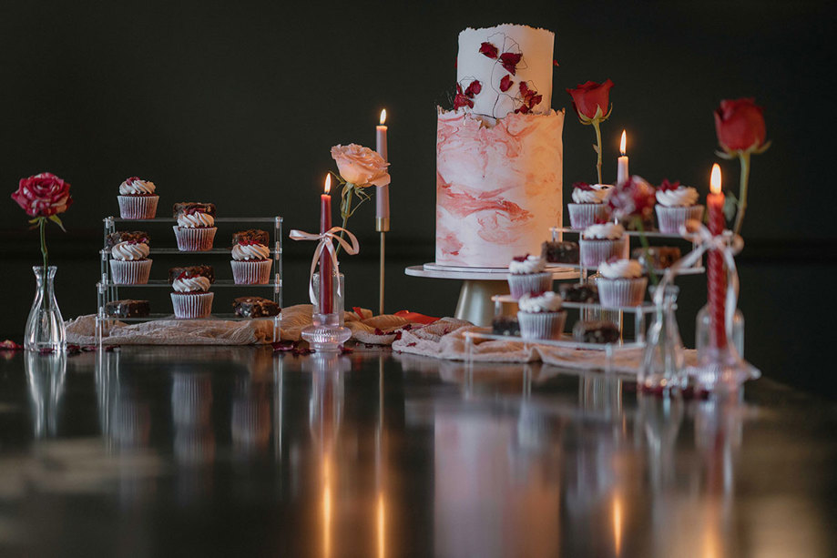 a two tier cake and a selection of cupcakes with white, pink and red icing designs 