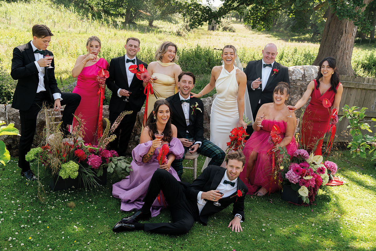 Wedding party at Kinkell Byre wearing colourful formal outfits in pink, red, purple and cream, surrounded by bright floral arrangements.