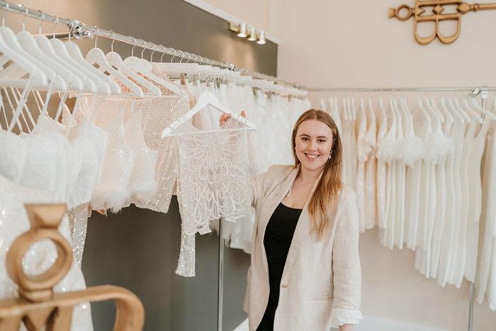 a woman holding up a sleeveless sparkly white top she's selected from a hanging store display