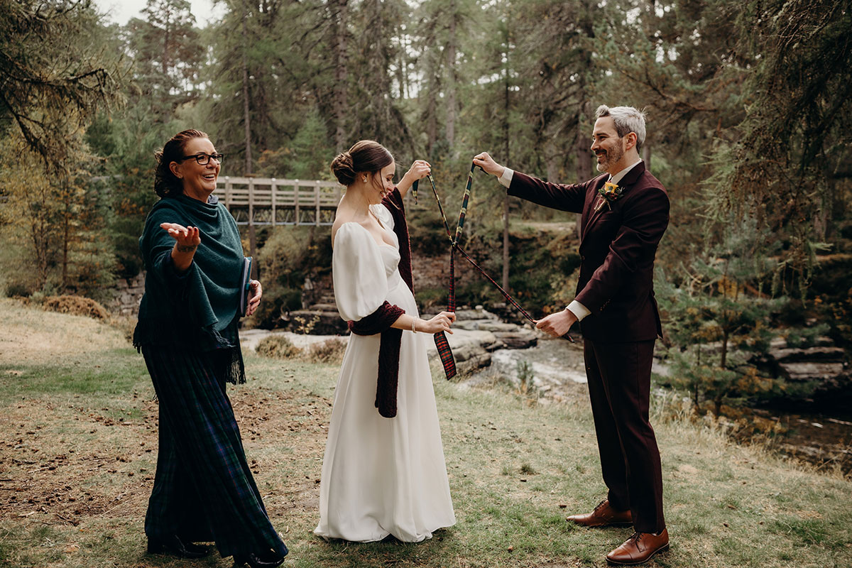 Outdoor wedding ceremony with tartan ribbon handfasting on River Quoich at Mar Lodge Estate